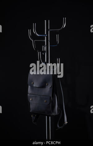 black leather backpack hanging on coat rack isolated on black Stock Photo