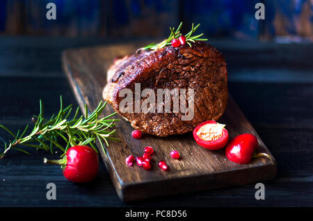 baked meat with rosemary and red pepper. steak. beef. dinner for men. dark photo. Black background. wooden board