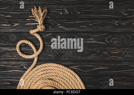 partial view of brown knotted nautical rope arranged in circle on wooden surface Stock Photo