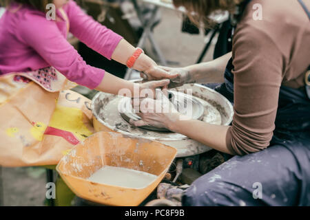 Female hands of potter and girl s hands . Master teaches the student to make pitcher on pottery wheel. Master class on modeling of clay on potter's wheel Stock Photo