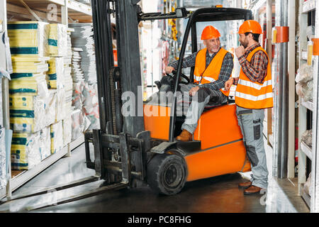two male workers using forklift machine in storehouse Stock Photo