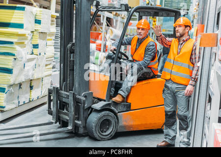worker and his senior colleague working with forklift machine in storage Stock Photo