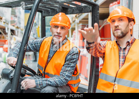 worker and his senior colleague working with forklift machine in storehouse Stock Photo