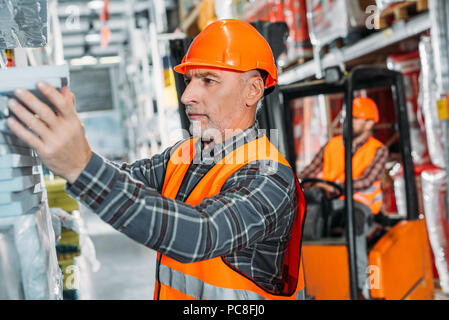 senior worker and his colleague working with forklift machine in storehouse Stock Photo