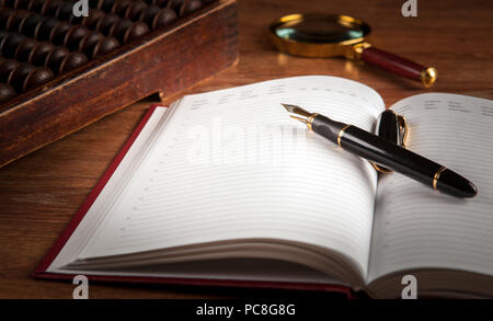 fountain pen and diary on a table with an abacus and loupe close up Stock Photo