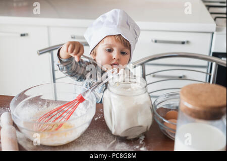 little kid in chef hat preparing dough at kitchen Stock Photo