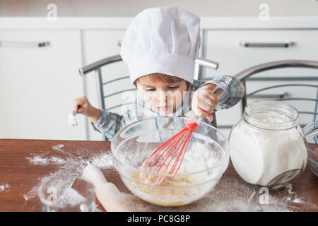 little kid in chef hat mixturing dough with whisk at kitchen Stock Photo