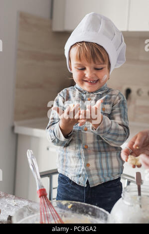 adorable little kid in chef hat looking at dirty hands covered with flour while cooking Stock Photo