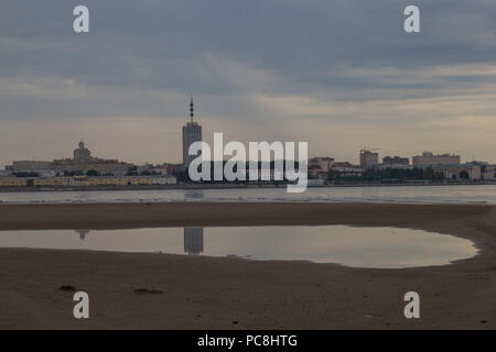 A view of the city of Arkhangelsk from the side of the river. Reflection of a skyscraper in a puddle on the beach. Stock Photo