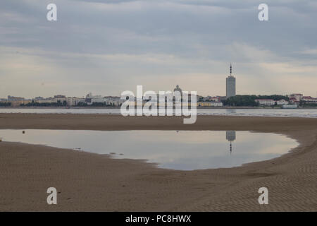 A view of the city of Arkhangelsk from the side of the river. Reflection of a skyscraper in a puddle on the beach. Stock Photo