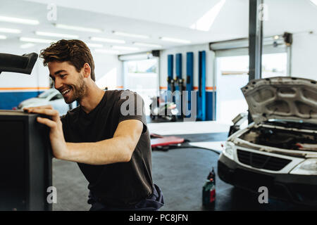 Smiling mechanic checking a car with computer in service station.  Mechanic doing computerized diagnostic of car. Stock Photo