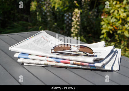 Pile of newspapers and sunglasses on a table in a garden during summer Stock Photo