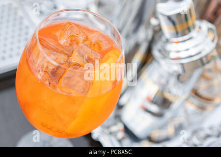 Aperol spritz cocktail in misted glass, selective focus. Alcoholic beverage based on bar counter with ice cubes and oranges. metal shakers in the background Stock Photo