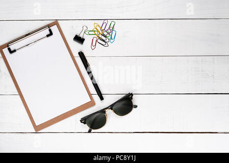 Blank notepad with fountain pen, miscellaneous paper clips and dark glasses over white wooden background Stock Photo