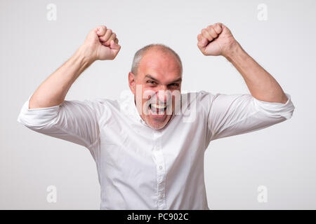Mature hispanic man is happy with his win. He is holding his fists and shout Wow. Stock Photo