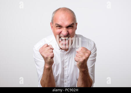Mature hispanic man is happy with his win. He is holding his fists and shout Wow. Stock Photo