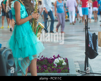 back view little girl standing in the crowded street and playing saxophone music Stock Photo