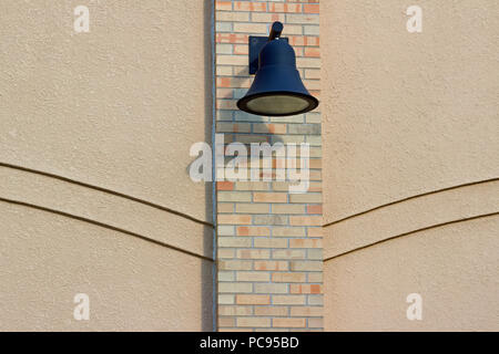 View of an attractive light colored brick and stone exterior wall featuring a black metallic building wall light or lamp, with simple decorative lines Stock Photo