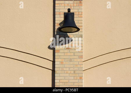 View of an attractive light colored brick and stone exterior wall featuring a black metallic building wall light or lamp, with simple decorative lines Stock Photo