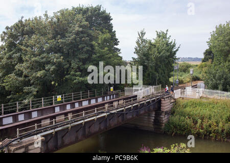 A senior couple walking across an unmanned railway level crossing, by a railway bridge over the River Tillingham, Rye, East Sussex. Stock Photo