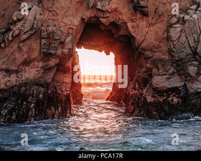 Stunning view of the Pacific Ocean through an opening in the rocky cliff at Pfeiffer Beach, near Big Sur, California. Rocks colored red by the sunset. Stock Photo