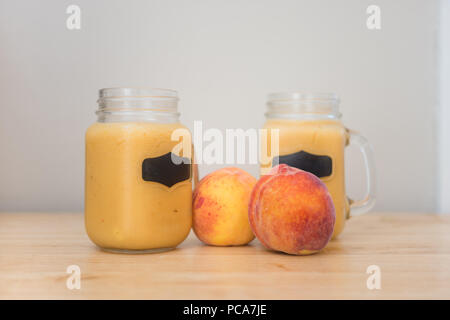 Glass jars with handles full of fresh peach puree next to large fresh