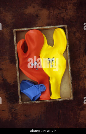 Three deflated party balloons with rabbit ears and faces lying in cardboard box Stock Photo