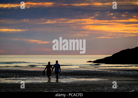 Couple walking on Porth Beach at Newquay in Cornwall at sunset Stock Photo