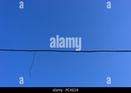 The black wire from the ragged end on plastic mounts against the blue sky Stock Photo