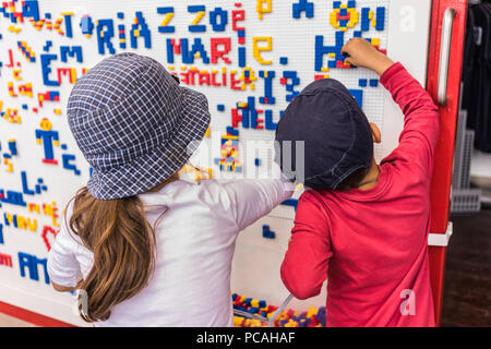 Close-up details of children playing along the wall full of names made from colorful puzzle blocks. Colorful abstract puzzle and letter details Stock Photo