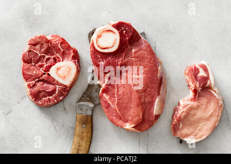 Set raw beef meat on bone and pork meat on white concrete background with butcher knife, top view Stock Photo