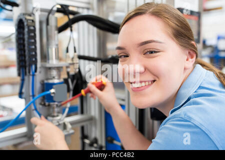 Portrait Of Female Apprentice Engineer Working On Machine In Factory Stock Photo