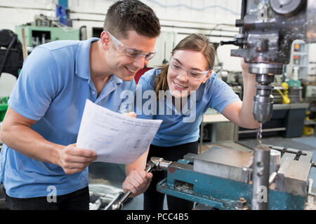 Engineer Instructing Female Apprentice On Use Of Drill Stock Photo