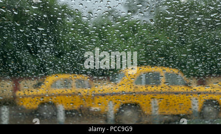 Raindrops falling on glass, abstract blurs - monsoon stock image of traditional yellow taxi of Kolkata ,West Bengal, India Stock Photo