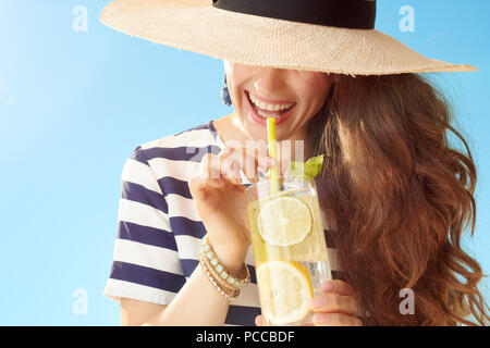 trendy woman in straw hat against blue sky drinking refreshing cocktail Stock Photo