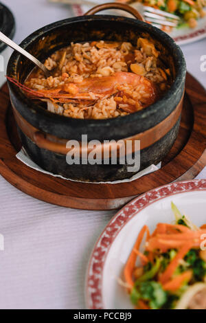 National cuisine of Cape Verde: Cachupa with prawn in traditional stone bowl with vegetable salad on a plate. Stock Photo