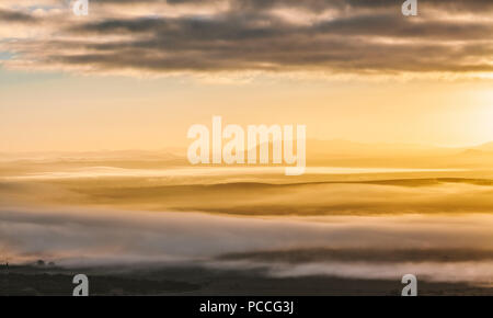 Beautiful glowing sunrise landscape - clouds laying low covering mountain silhouettes Stock Photo