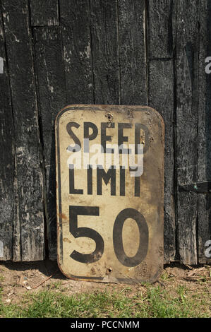 Old vintage grungy speed limit 50km road sign Canadian.  In front of old black painted barn board garage door peeling paint and grass. Stock Photo