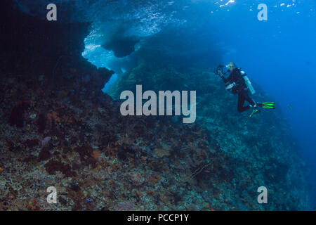 Female scuba diver with video camera photographs the backside of Boo Windows. Raja Ampat, Indonesia. Stock Photo