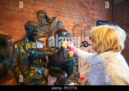 Sue Stopps (white coat), wife of David Stopps (not pictured), attempts to clean the statue of David Bowie in Aylesbury after it was vandalised days after being unveiled Stock Photo