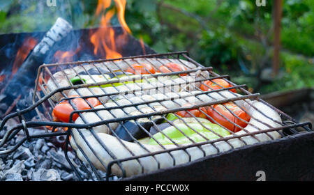 Pork sausages with vegetables are grilled on fire. Cooking dinner outdoors. Stock Photo