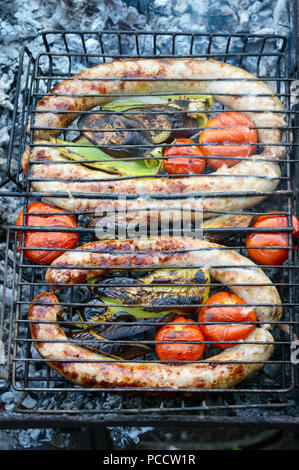 Pork sausages with vegetables are grilled on fire. Cooking dinner outdoors. Stock Photo