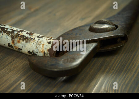 Vintage rusty pipe wrench on pipe on dark wooden background, symbolic of plumbing trade with low angle selective focus and copy space Stock Photo