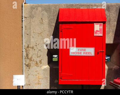 Red fire hose reel, mounted on old concrete wall background Stock Photo