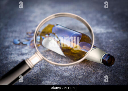 Shattered beer bottle resting on the ground seen through a magnifying glass - alcoholism concept image Stock Photo