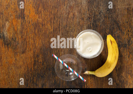 Banana milkshake in plastic cup on wooden background. Top view with copy space Stock Photo