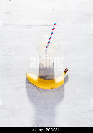 Banana milkshake in plastic cup on white wooden table Stock Photo