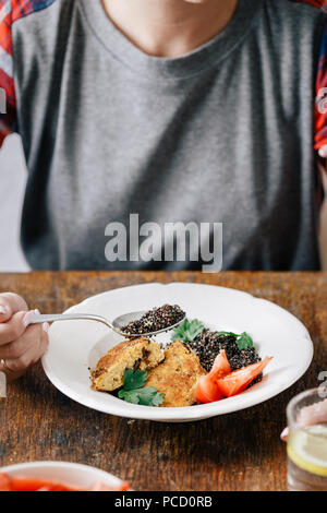 Woman eating vegetarian food (black quinoa and cutlets from oatmeal and prunes). Healthy vegetarian food concept Stock Photo