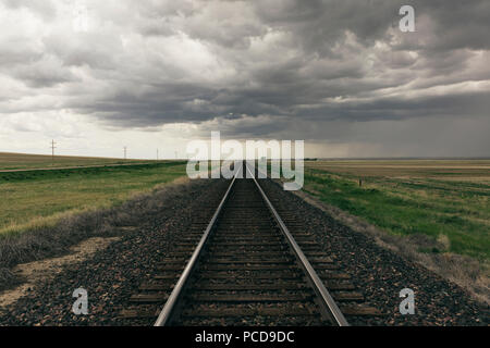 Train tracks through prairie and farmland, storm clouds in distance Stock Photo