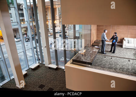 A large building, lobby, view looking into an office with glass walls, two business people talking. Stock Photo